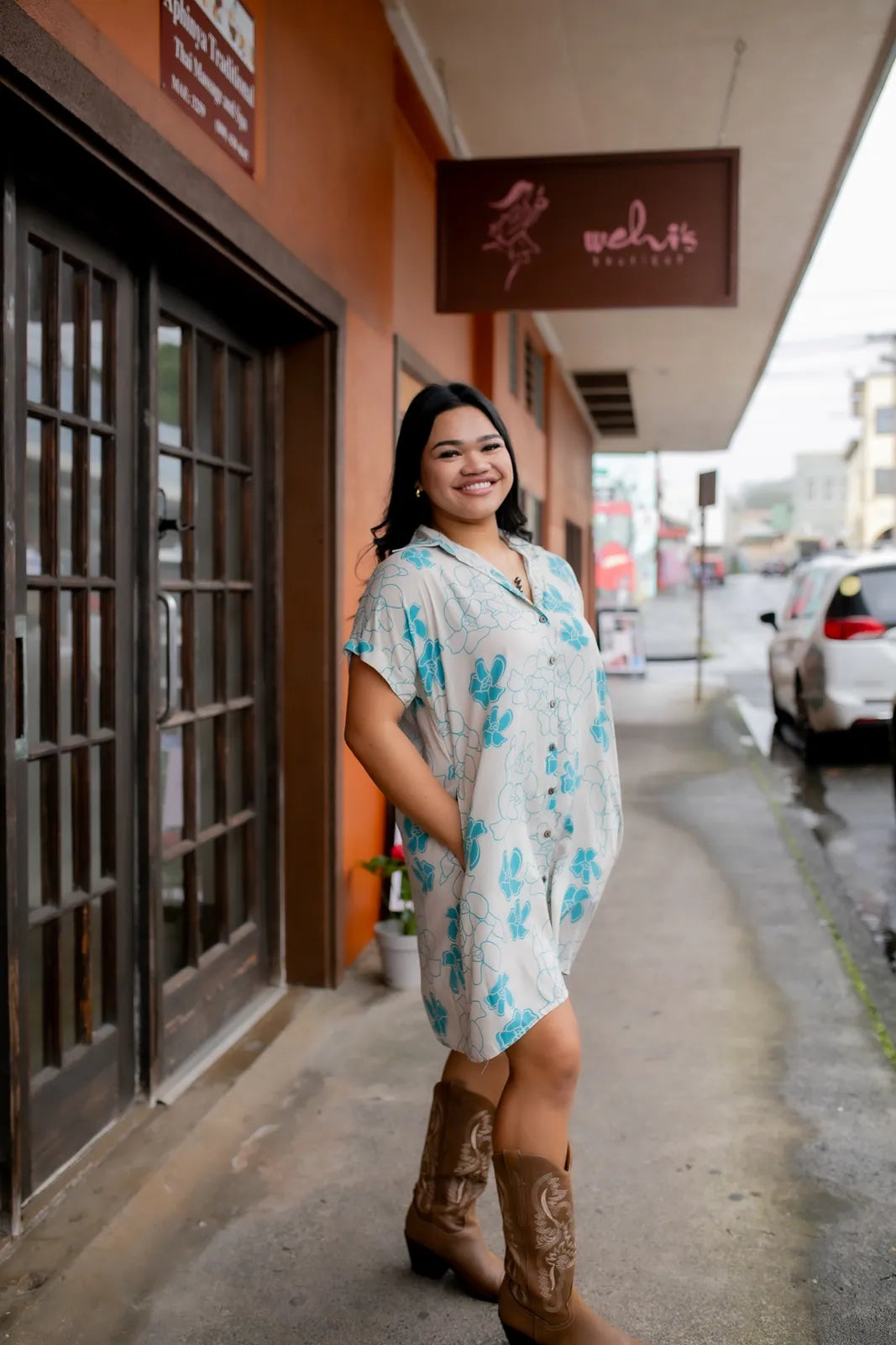 A wāhine in a Wehi print dress and paniolo boots outside the Wehi's Boutique storefront on Hawaiʻi Island