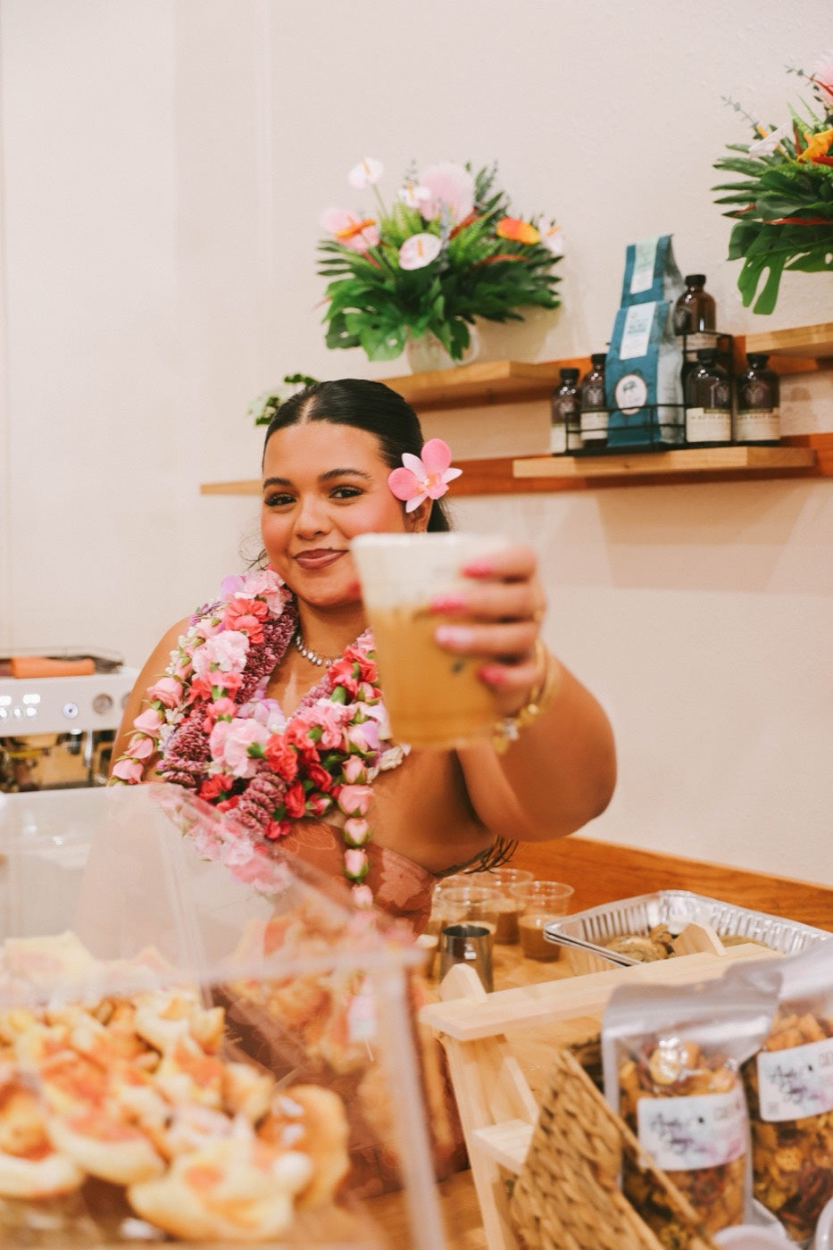 A SipNPretty barista holding out an iced latte at the café in Wehi's Hilo flagship